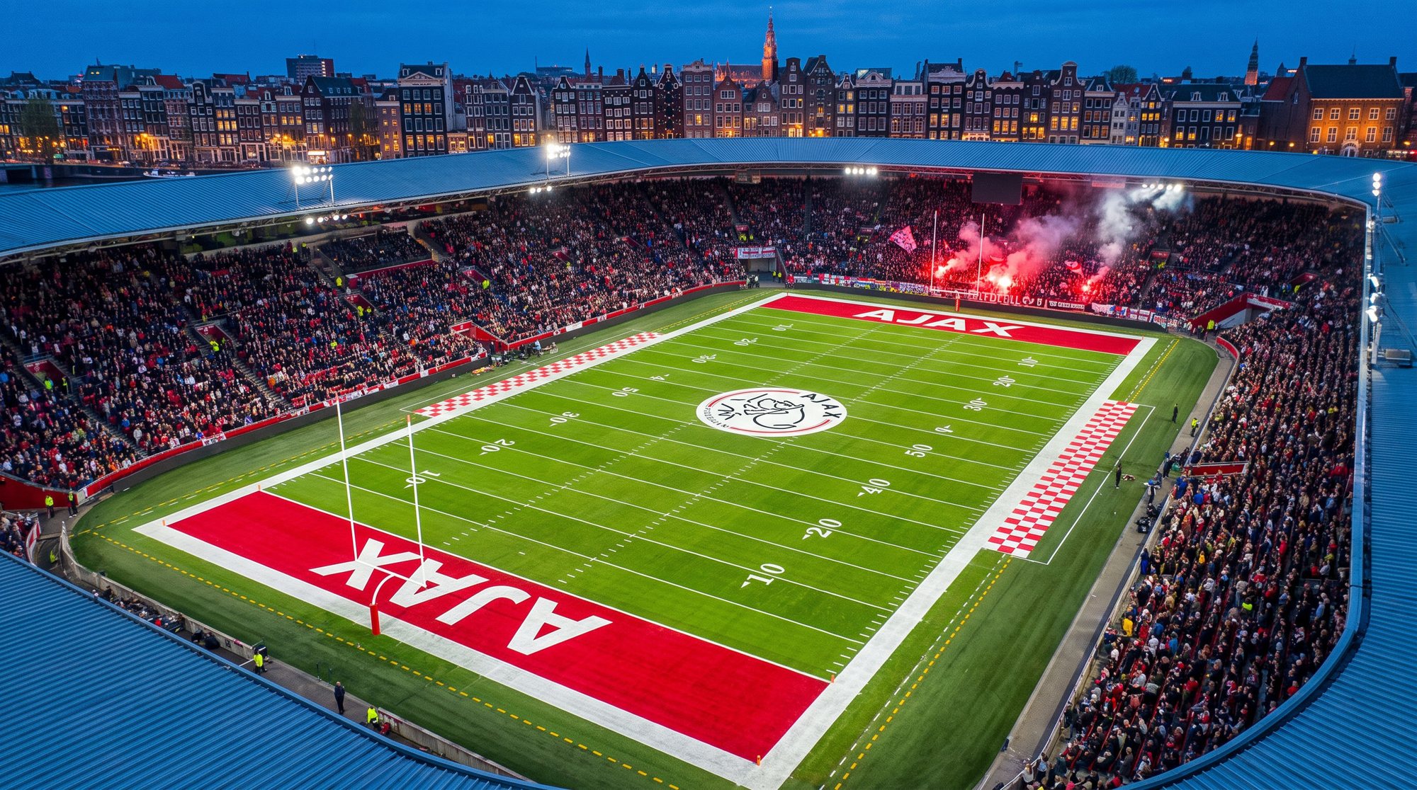 Blue-hour drone view of the Amsterdam stadium with an American football field: red AJAX end zones, crest at midfield, flares in the far stand and canal houses beyond