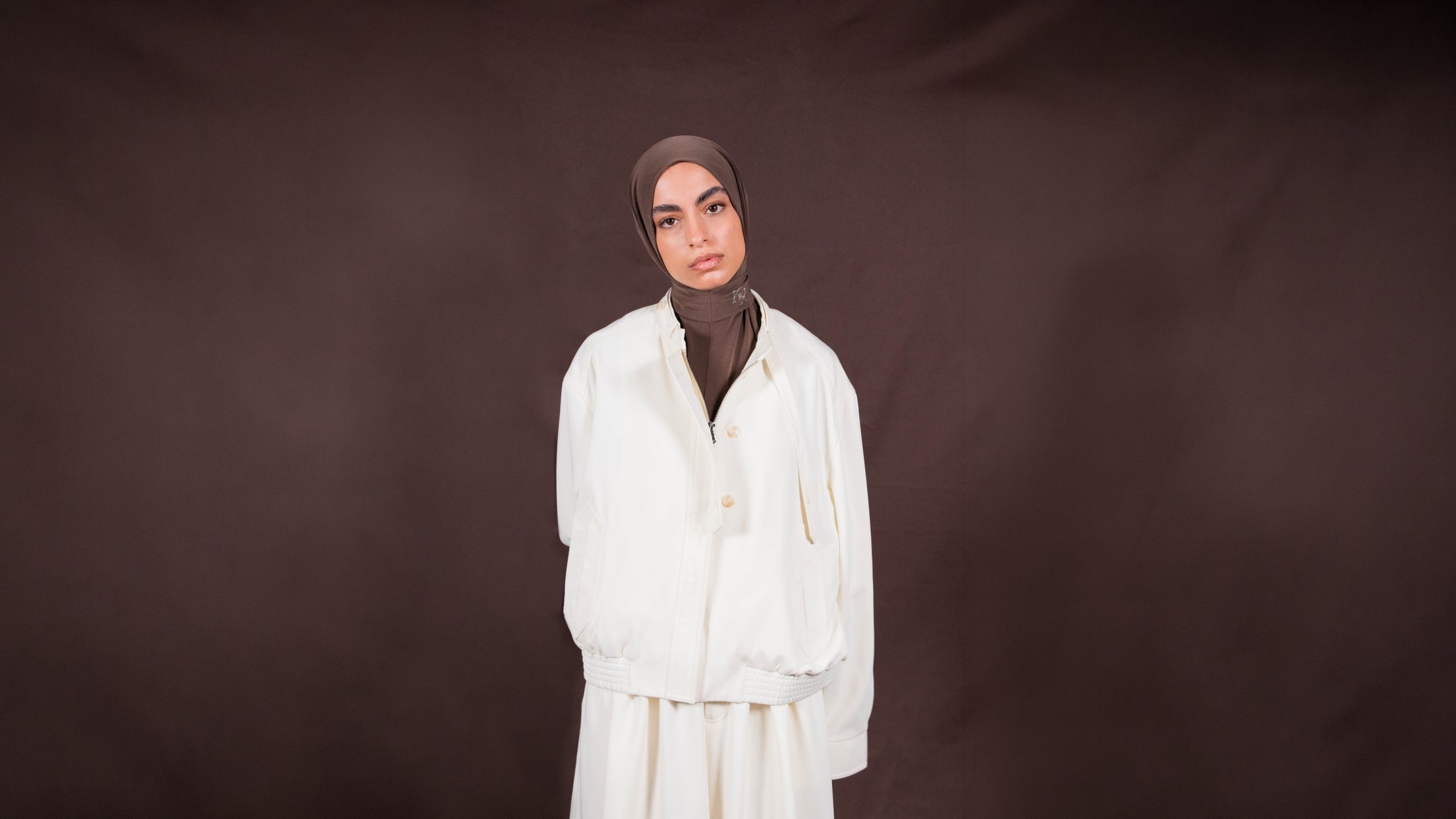 Kallouchi homepage hero: the model in a brown hijab and ivory jacket against a brown backdrop