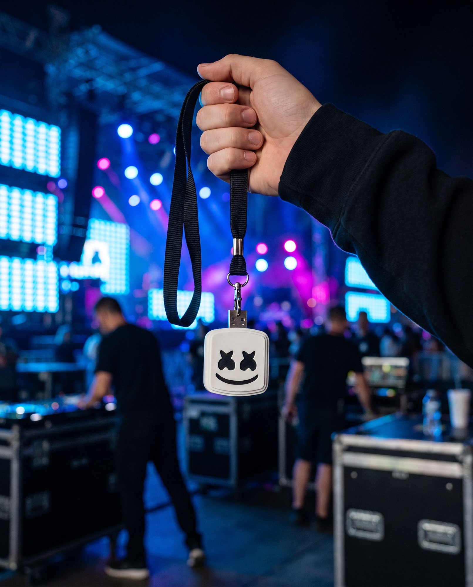 A hand holding up the white marshmallow USB stick on a black lanyard backstage at a festival